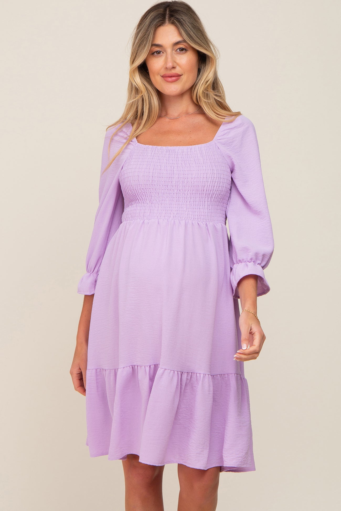 woman wearing a lavender maternity dress with a square neckline, smocked bodice, and bell sleeves