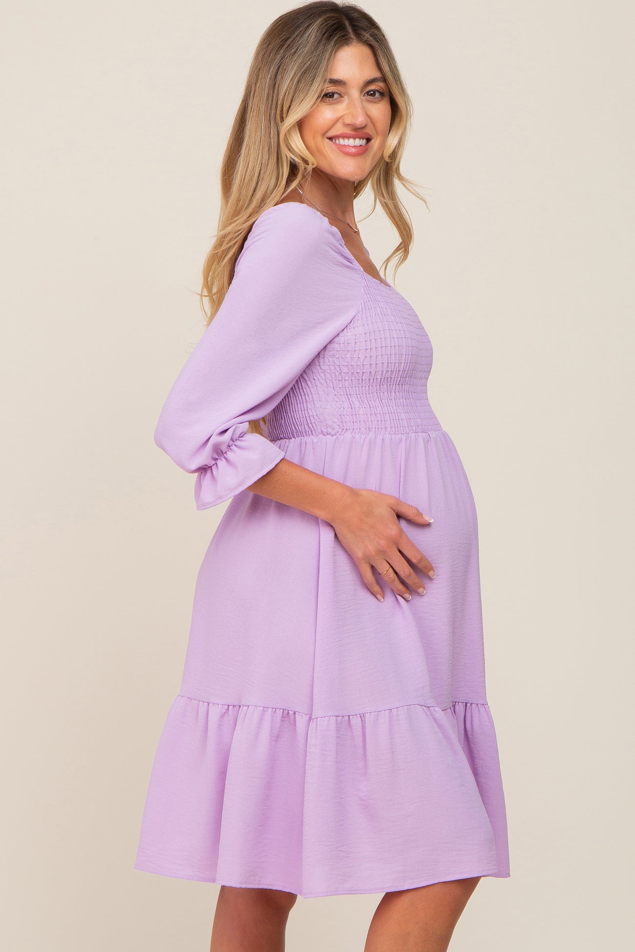 woman wearing a lavender maternity dress with a smocked bodice and ruffled hem, showing her baby bump