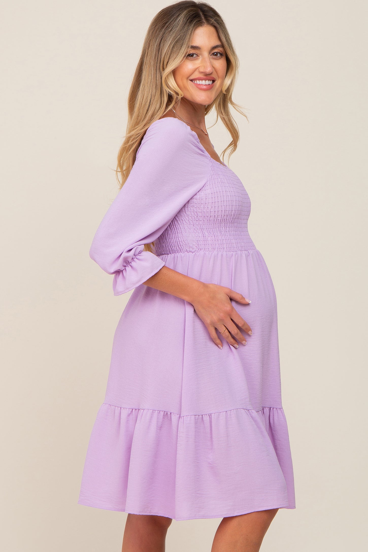 woman wearing a lavender maternity dress with a smocked bodice and ruffled hem, showing her baby bump