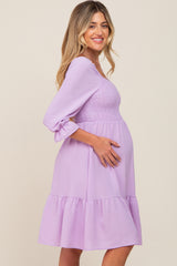 woman wearing a lavender maternity dress with a smocked bodice and ruffled hem, showing her baby bump