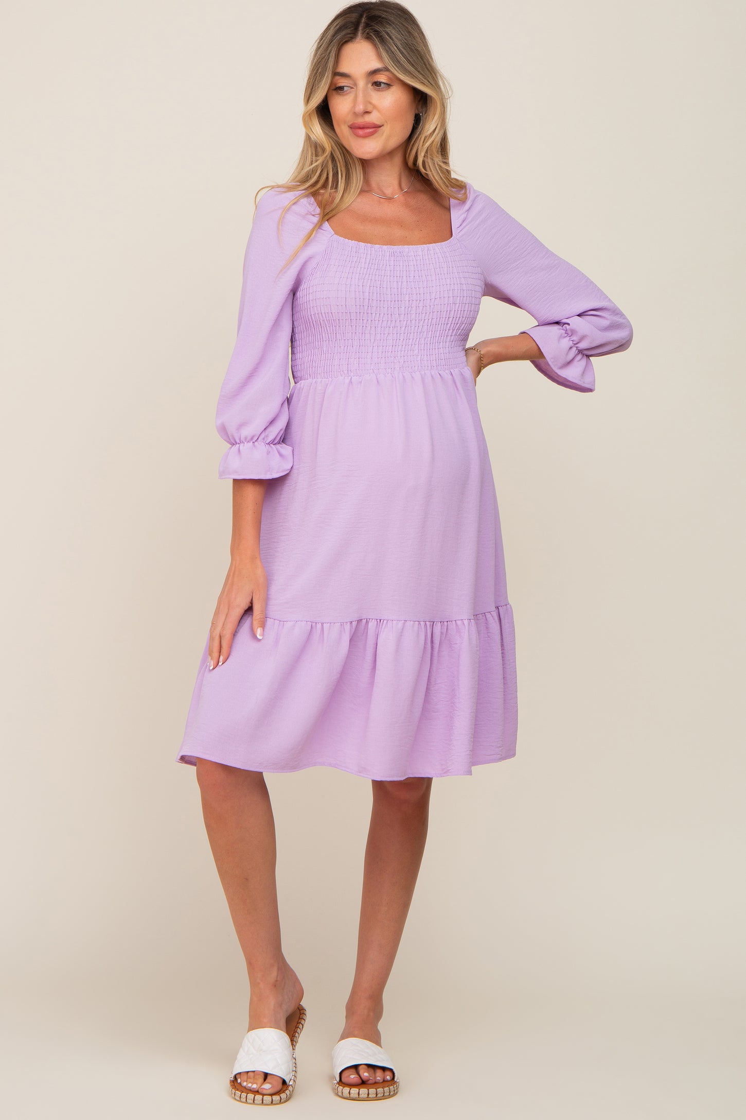 woman wearing a light purple maternity dress with a square neckline, smocked bodice, and tiered hem, highlighting her baby bump