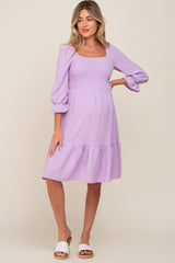 woman wearing a light purple maternity dress with a square neckline, smocked bodice, and tiered hem, highlighting her baby bump