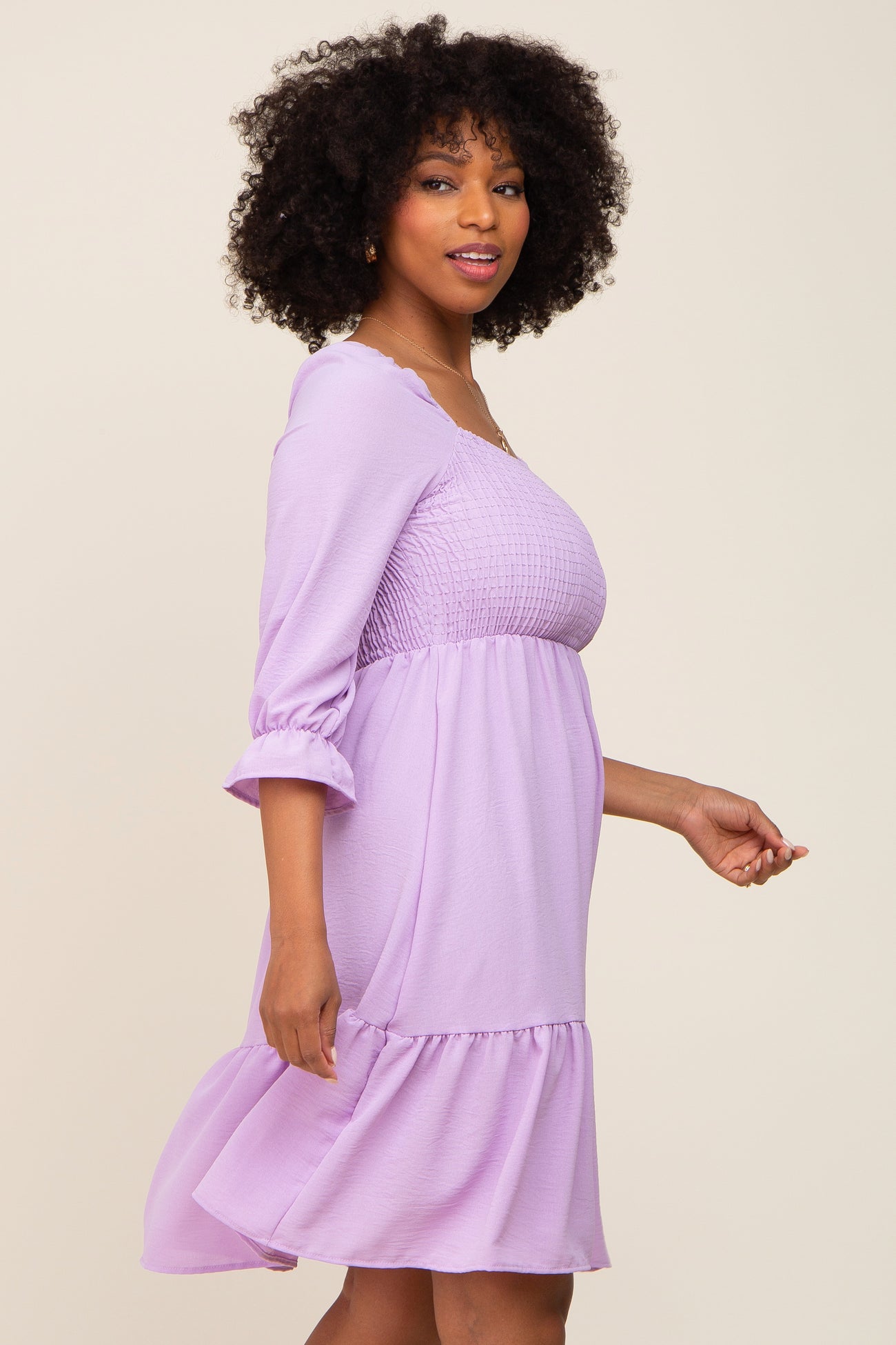 woman wearing a lavender smocked waist dress with three-quarter sleeves and a ruffled hem