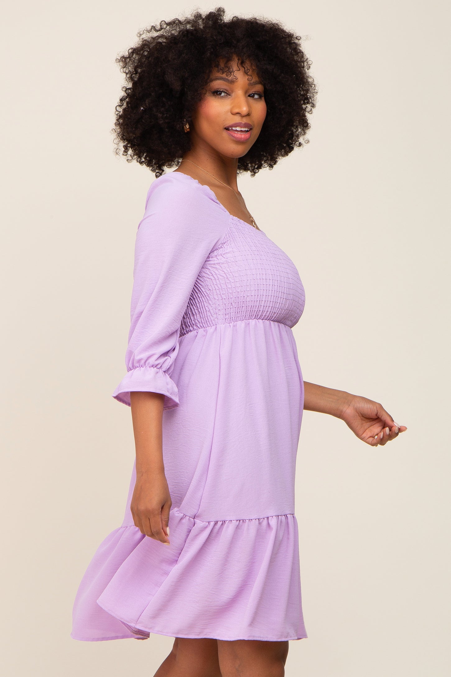 woman wearing a lavender smocked waist dress with three-quarter sleeves and a ruffled hem