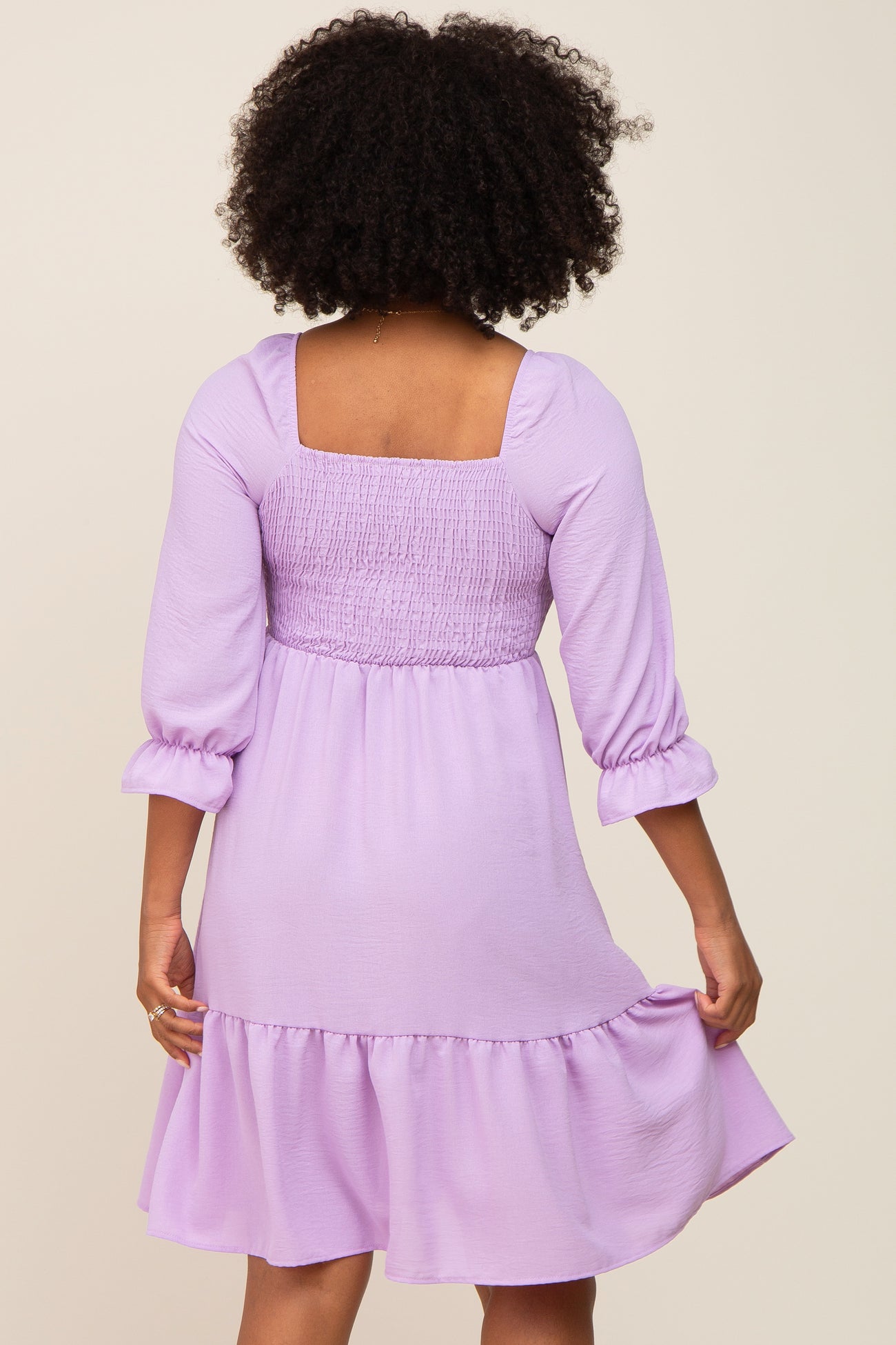 woman wearing a lilac smocked back dress with three-quarter sleeves and a ruffled hem