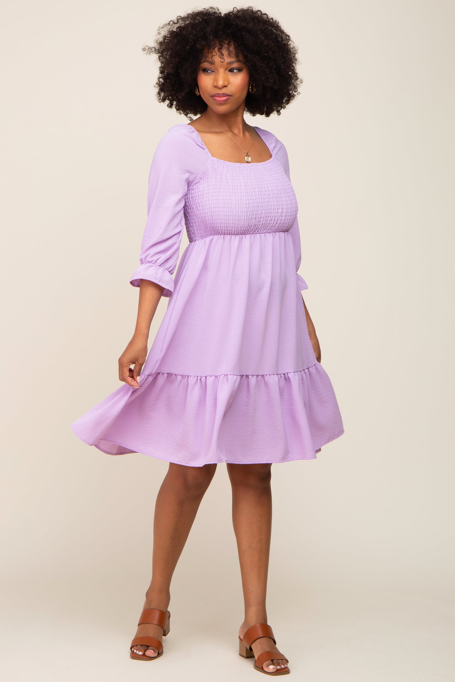 woman wearing a lilac smocked waist dress with three-quarter sleeves and a tiered ruffle hem