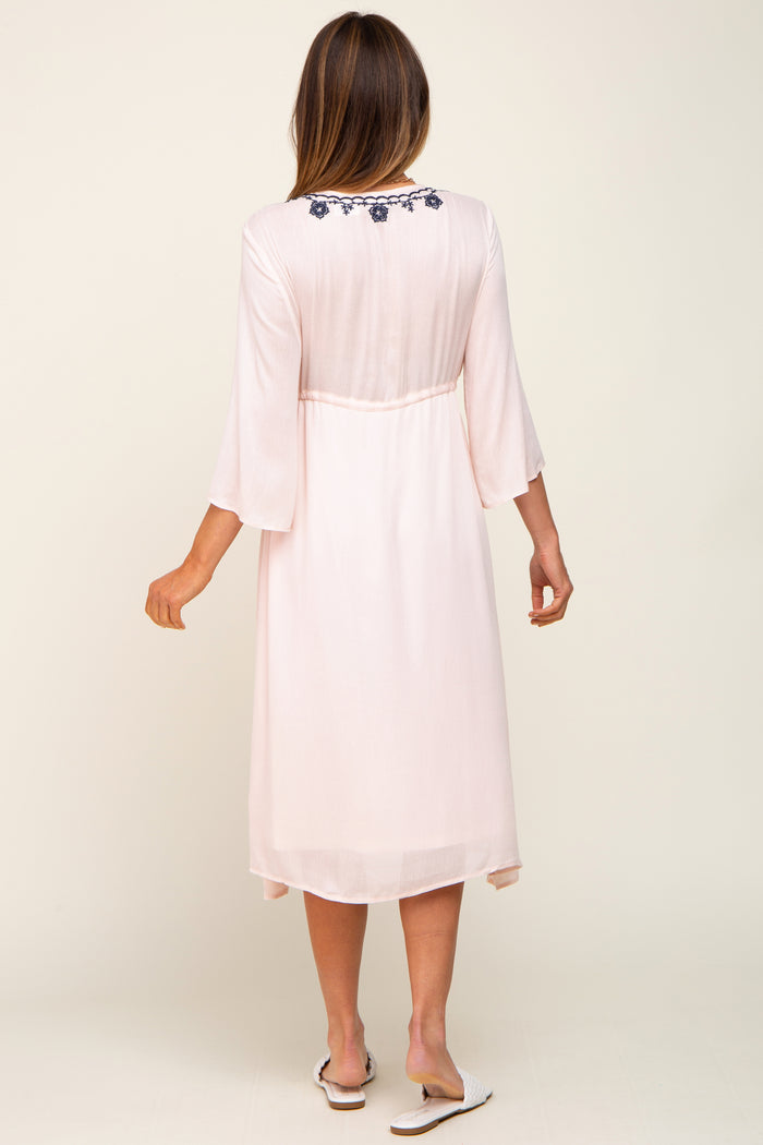 woman wearing a light pink maxi dress with three-quarter sleeves and embroidered details on the back