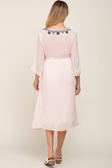 Back view of a woman wearing a light pink midi dress with navy blue floral embroidery on the neckline