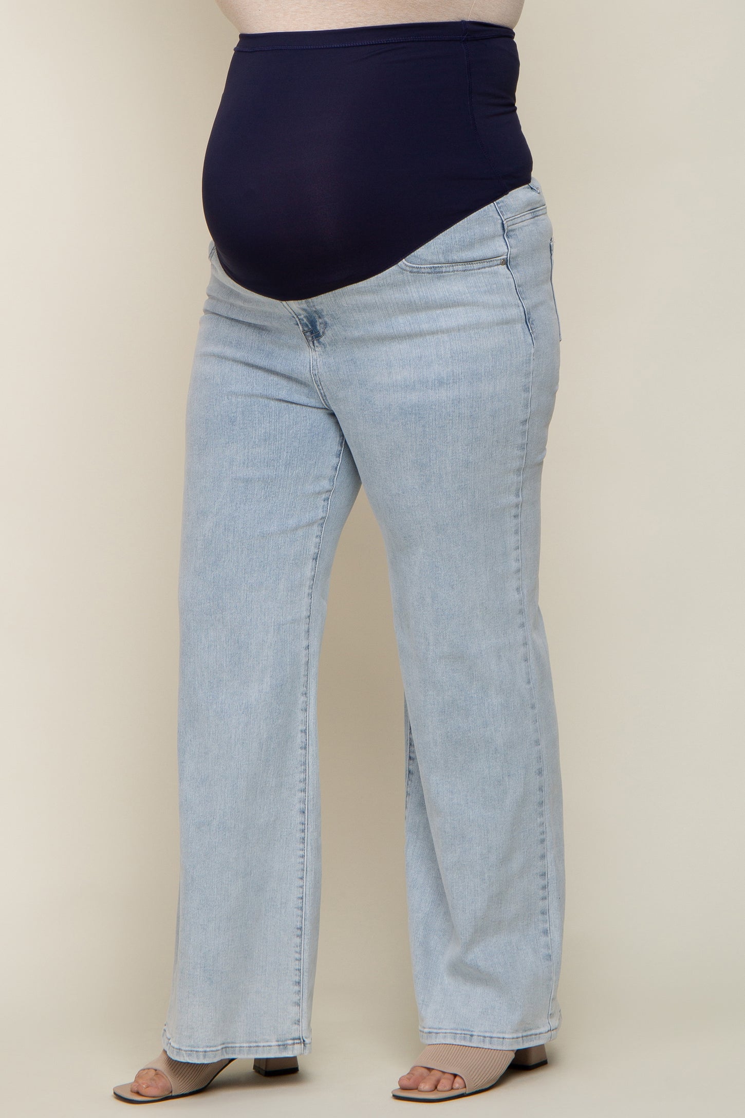 woman wearing light blue maternity plus jeans with a navy blue over-the-bump waistband and flared leg style