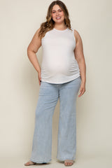 woman wearing a light beige sleeveless maternity top and light blue flared jeans, showing her baby bump