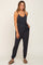 woman wearing a dark gray sleeveless jumpsuit with a tie waist and tapered legs, styled with sandals