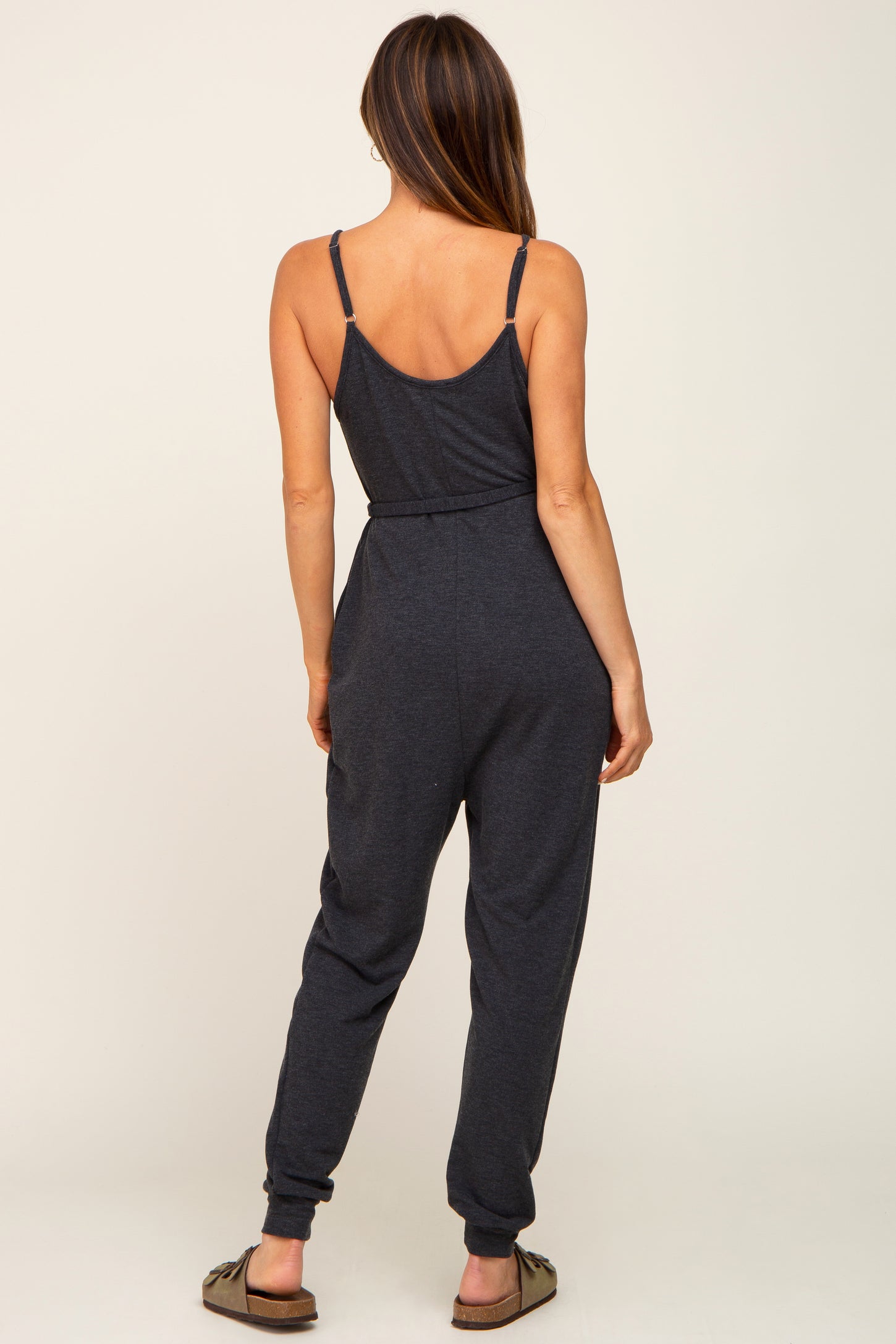 woman wearing a dark gray sleeveless jumpsuit with a cinched waist and tapered legs, shown from the back