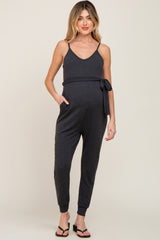 woman wearing a dark gray maternity jumpsuit with a tie waist and pockets, showcasing her baby bump