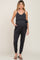 woman wearing a dark gray maternity jumpsuit with a tie waist and pockets, showcasing her baby bump