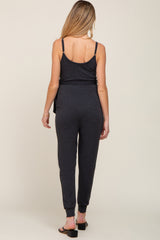 woman wearing a dark gray maternity jumpsuit, showing the back view with tapered legs and adjustable straps