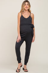 woman wearing a dark gray maternity jumpsuit with a tie waist and adjustable straps, showing a baby bump
