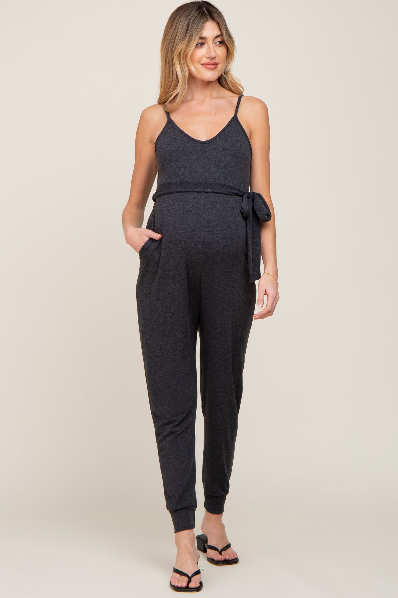 woman wearing a black maternity jumpsuit with adjustable straps and a tie at the waist, showing her baby bump