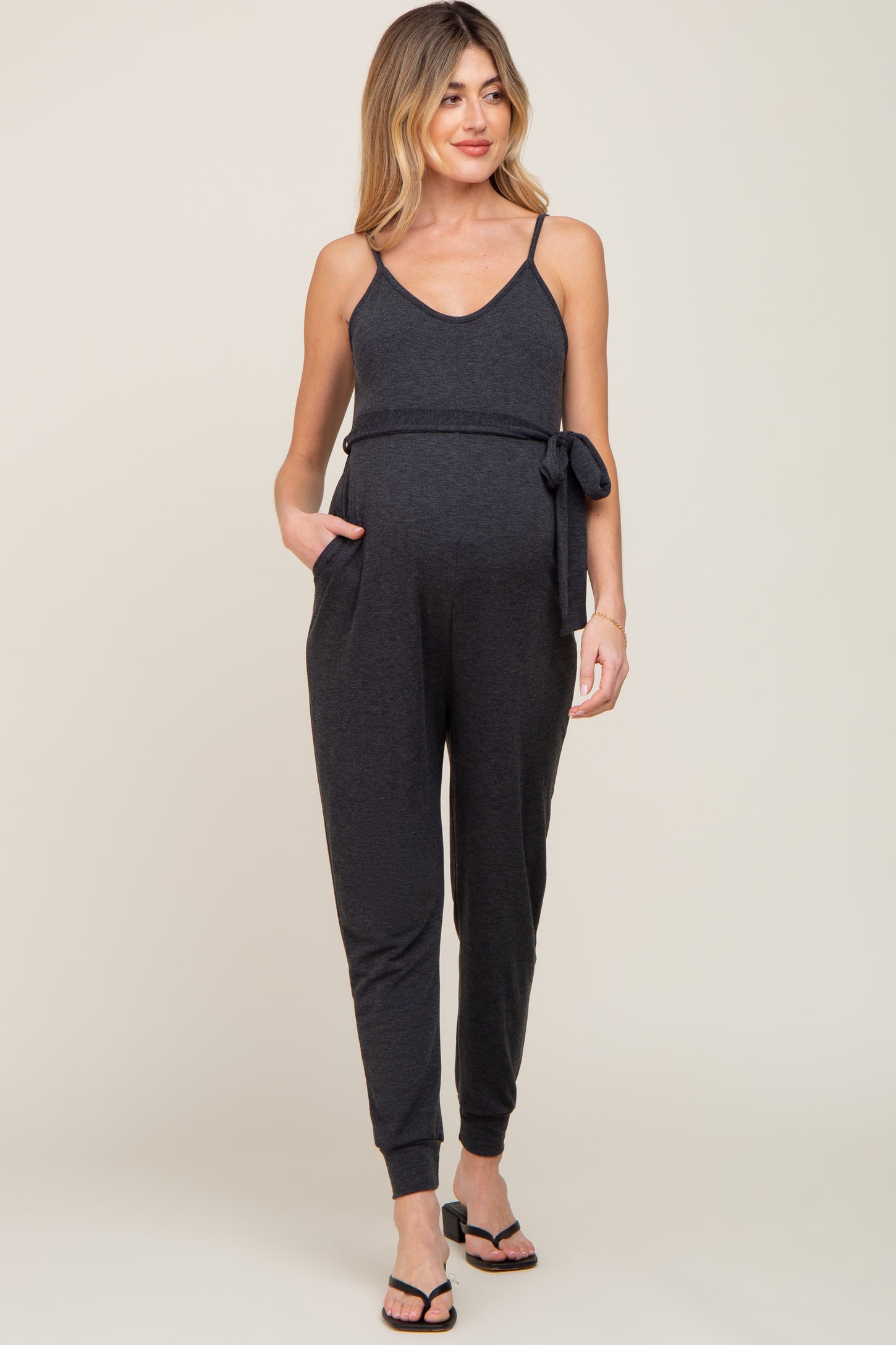 woman wearing a black maternity jumpsuit with adjustable straps and a tie at the waist, showing her baby bump
