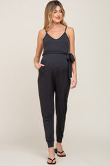 woman wearing a black maternity jumpsuit with adjustable straps and a tie at the waist, showing her baby bump