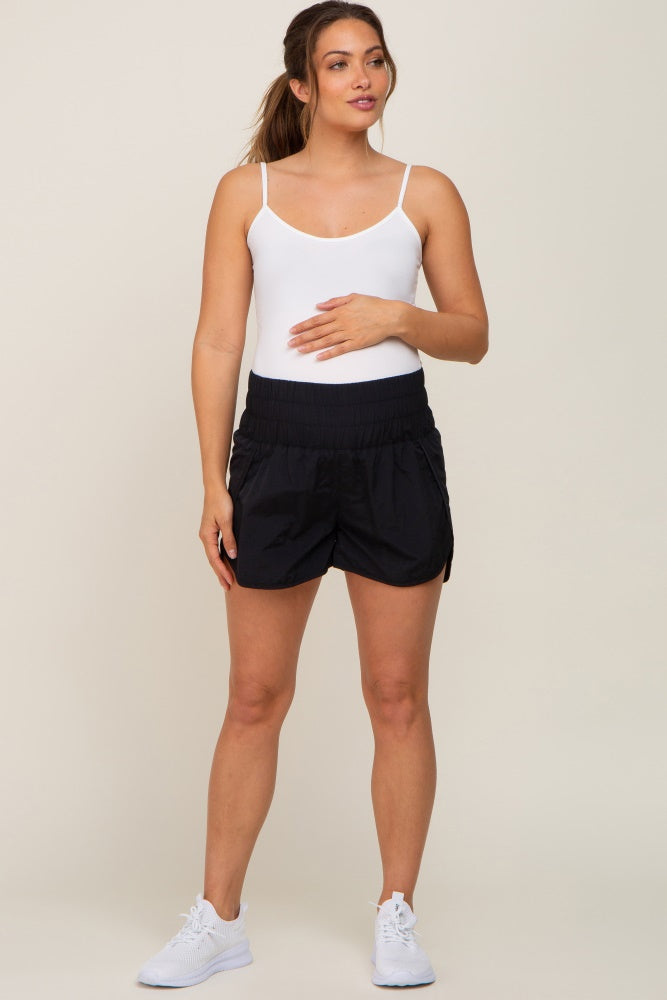 woman wearing a white tank top and black maternity shorts, holding her baby bump