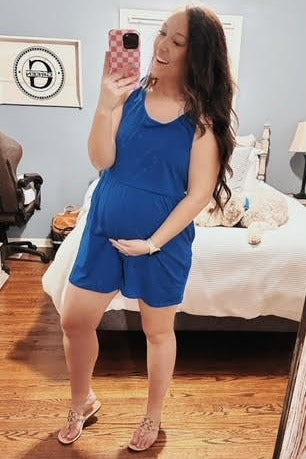 woman wearing a bright blue maternity romper and holding her baby bump
