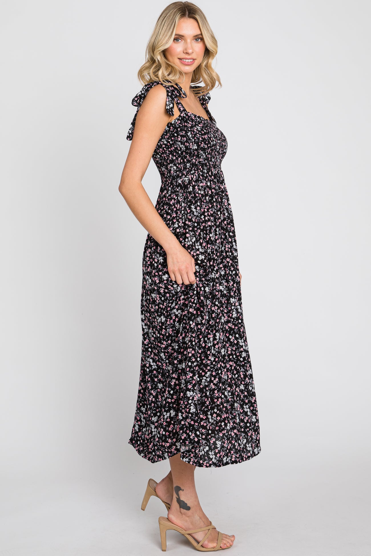 woman wearing a black floral midi dress with tie straps and a fitted bodice, styled with beige heeled sandals