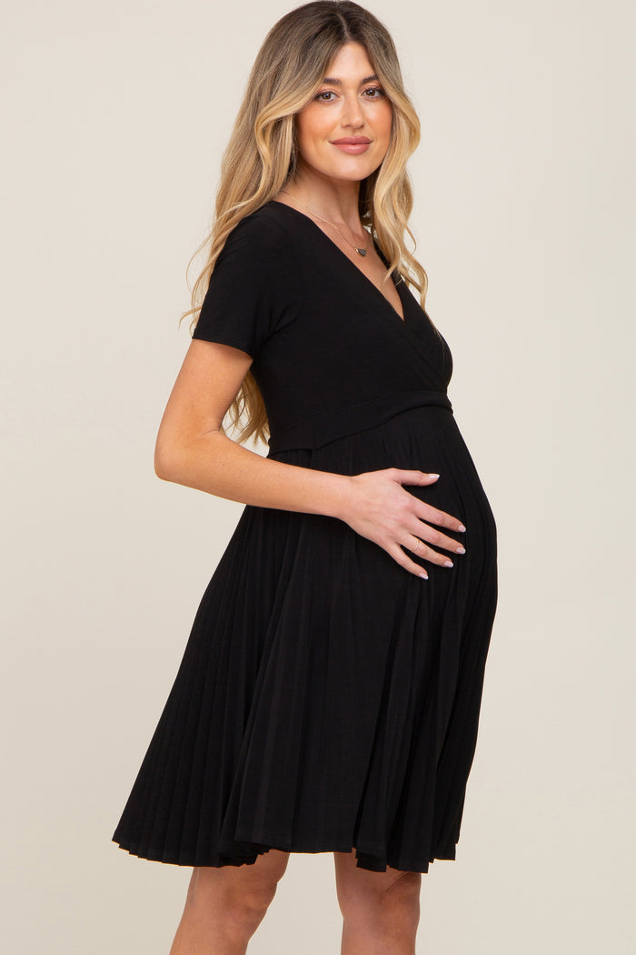 woman wearing a black short sleeve pleated maternity dress and cradling her baby bump