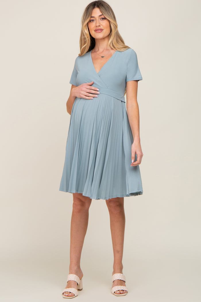 woman wearing a light blue short sleeve maternity dress with a pleated skirt and visible baby bump
