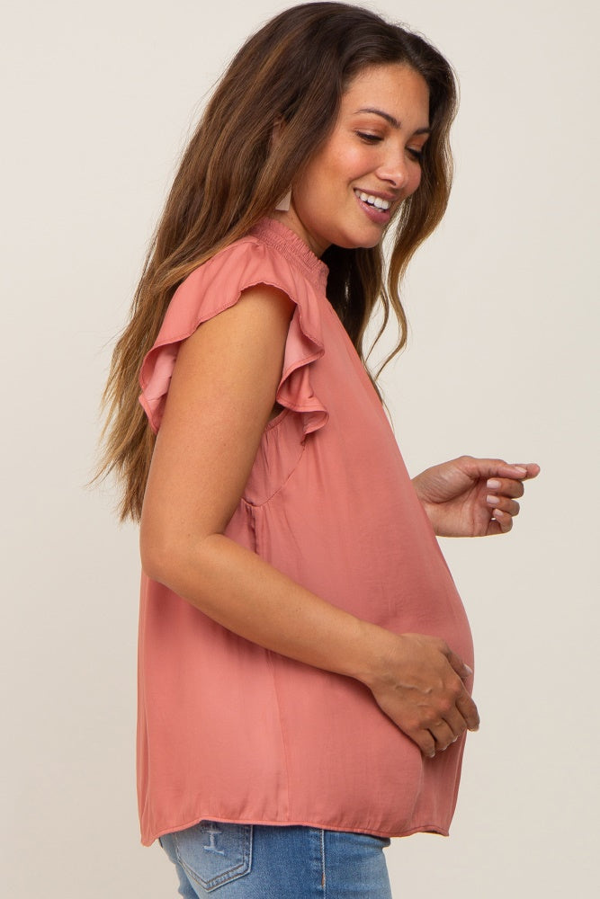 smiling pregnant woman wearing a rose pink ruffle sleeve maternity top and blue jeans