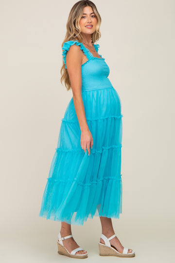 woman wearing a bright blue tiered maternity dress with ruffled straps and a visible baby bump, standing sideways