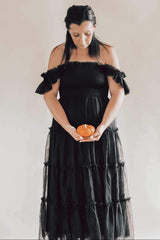 pregnant woman in black off-the-shoulder dress holding a small orange pumpkin over her belly