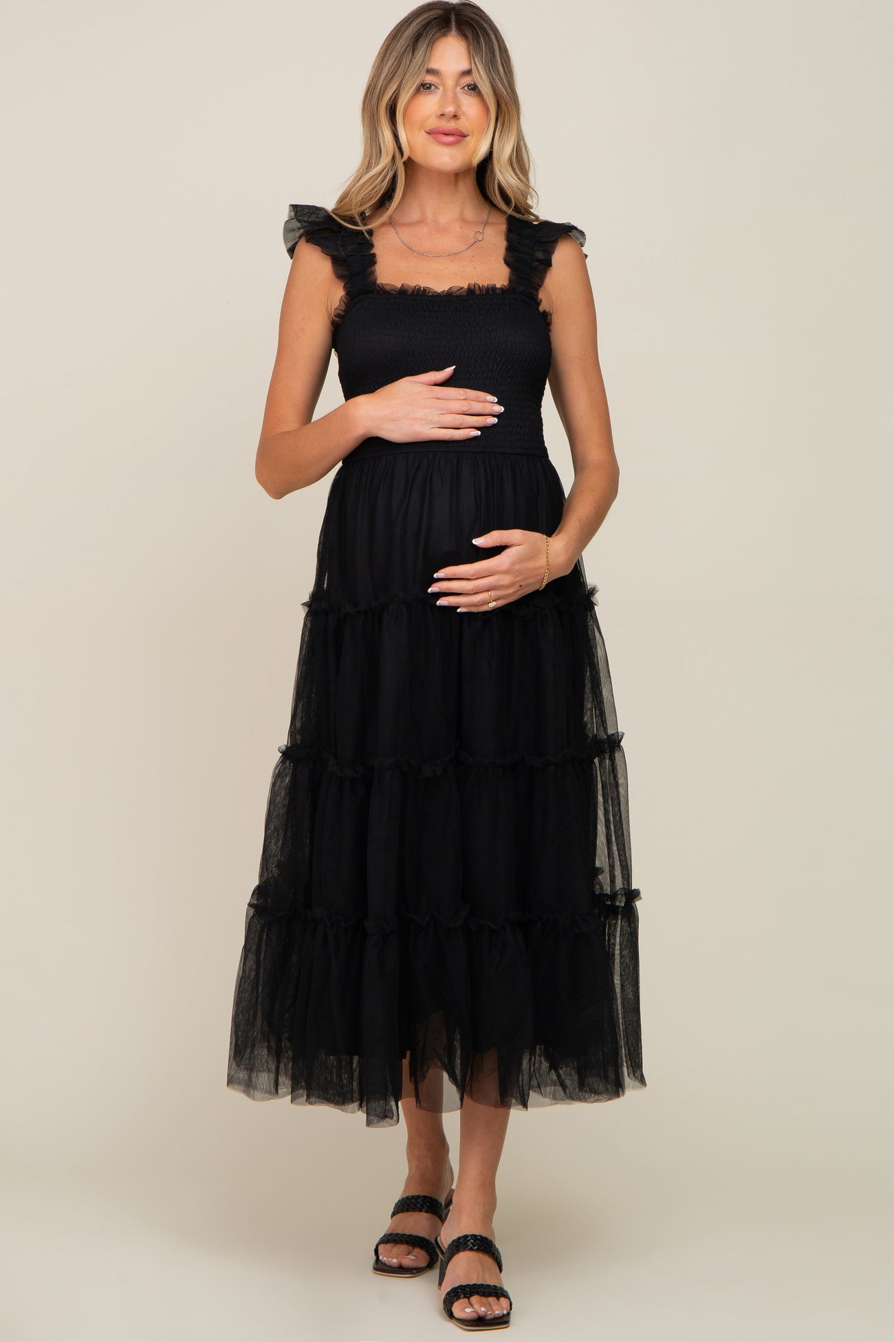woman wearing a black maternity dress with ruffle straps and tiered tulle skirt, holding her baby bump