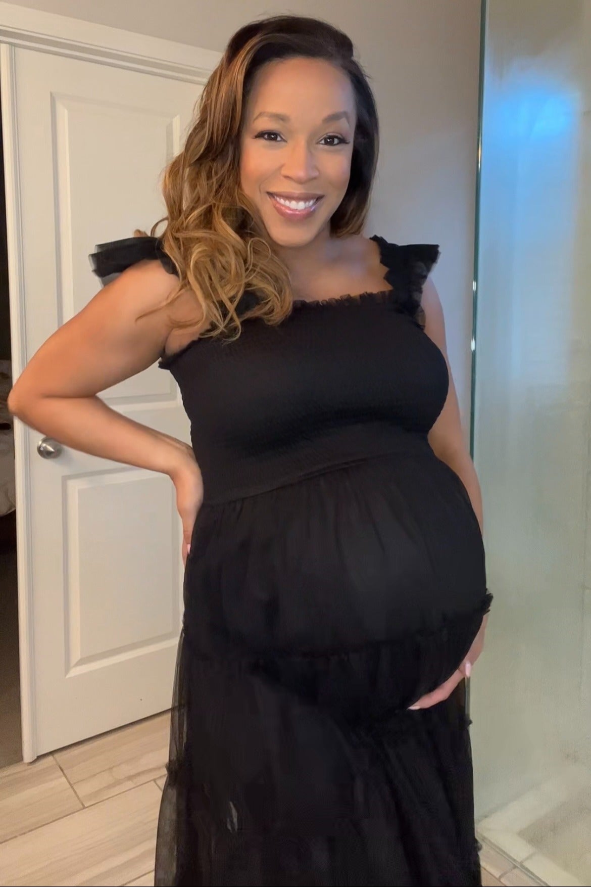 woman wearing a black maternity dress with ruffle straps and a visible baby bump
