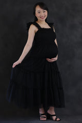 woman wearing a black tiered maternity dress with ruffled straps and showing her baby bump