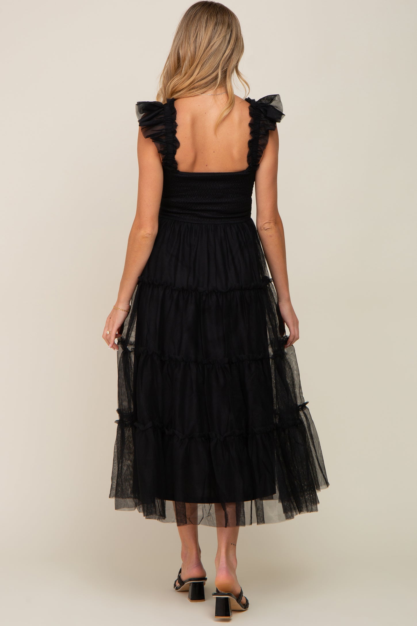 woman wearing a black maternity dress with ruffled sleeves and a tiered tulle skirt, seen from the back