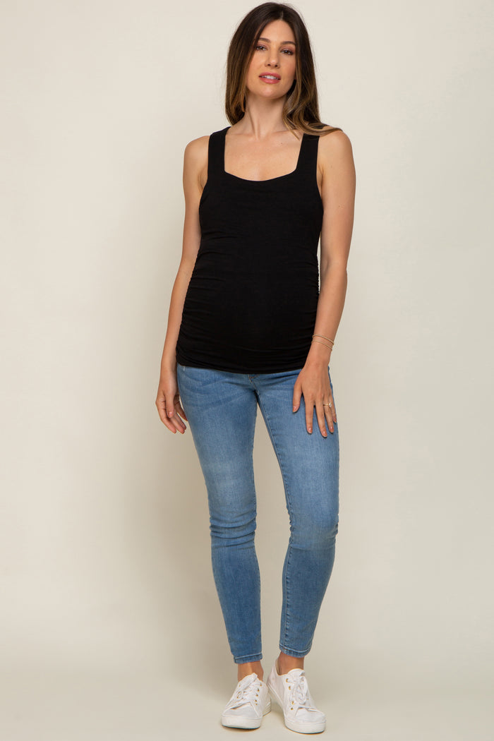 woman wearing a black maternity tank top and blue skinny jeans, showcasing a visible baby bump