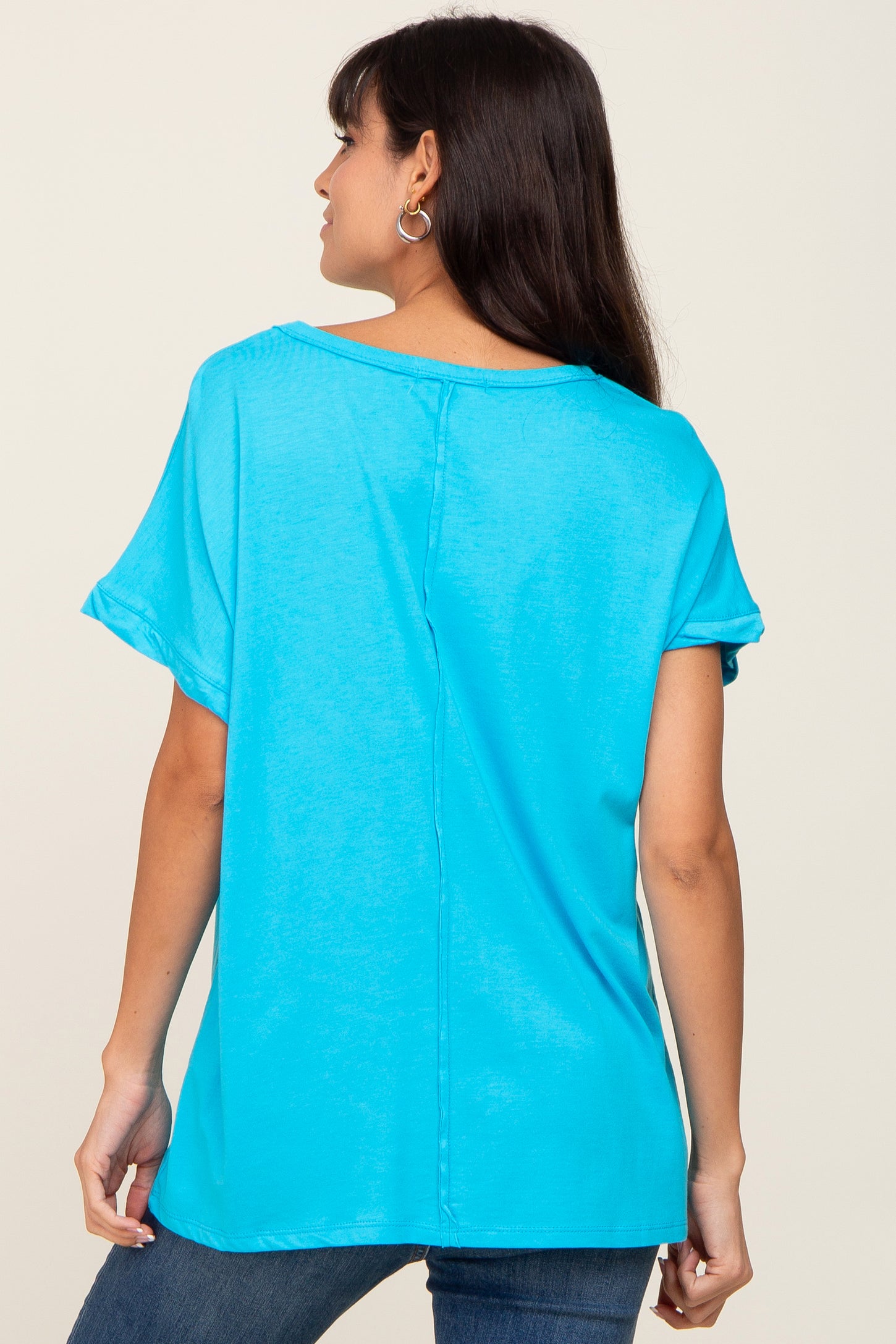 woman wearing a bright turquoise short sleeve top with rolled sleeves and a relaxed fit