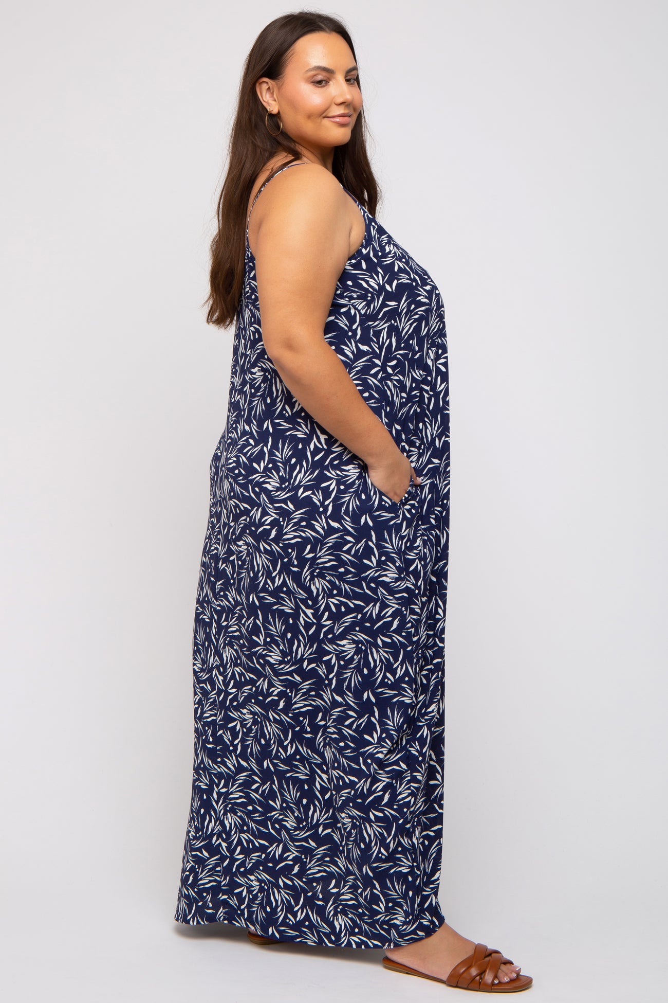 woman wearing a navy blue floral print maxi dress with pockets and sandals, shown from the side