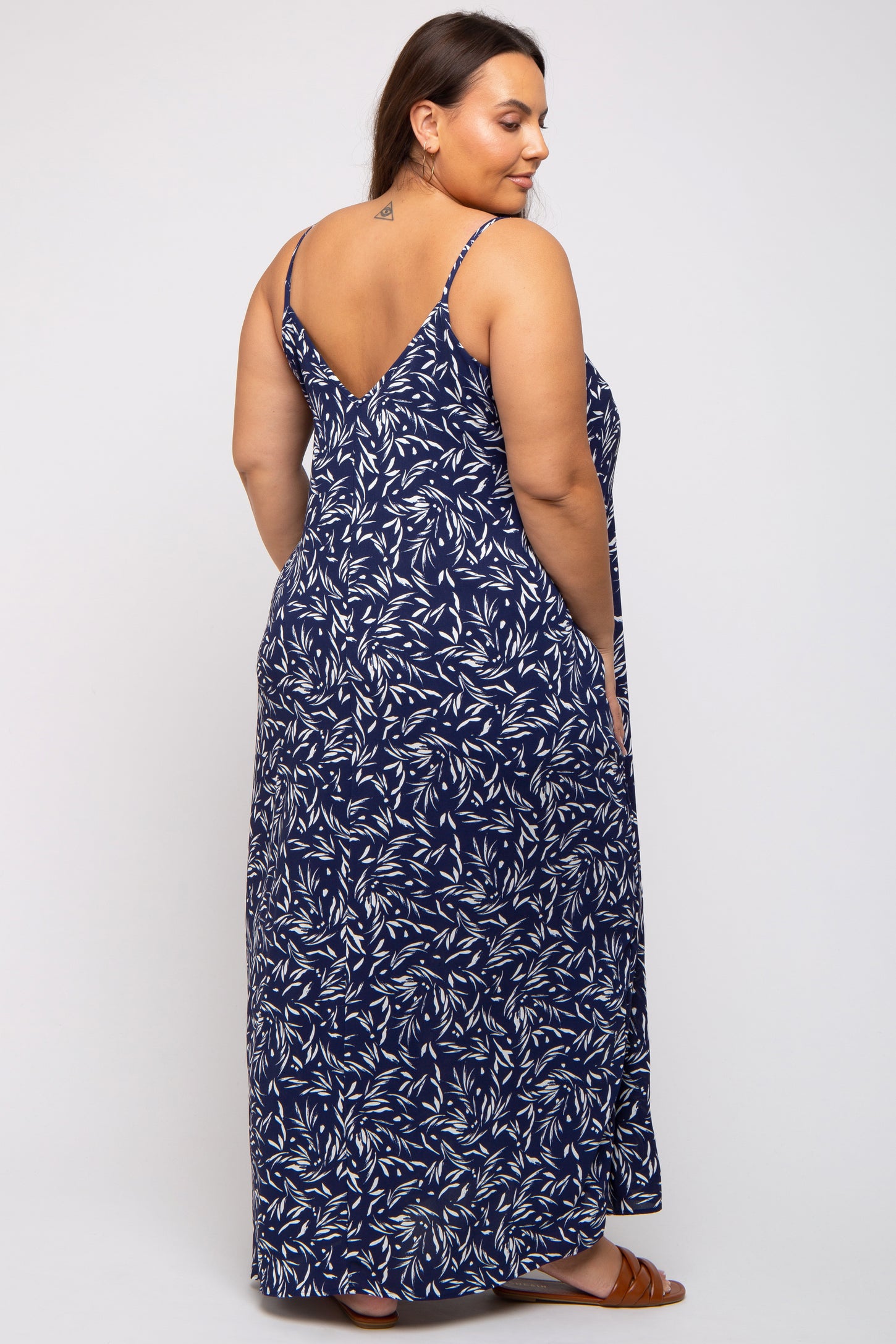 woman wearing a navy maxi dress with a leaf pattern and adjustable spaghetti straps, shown from the back