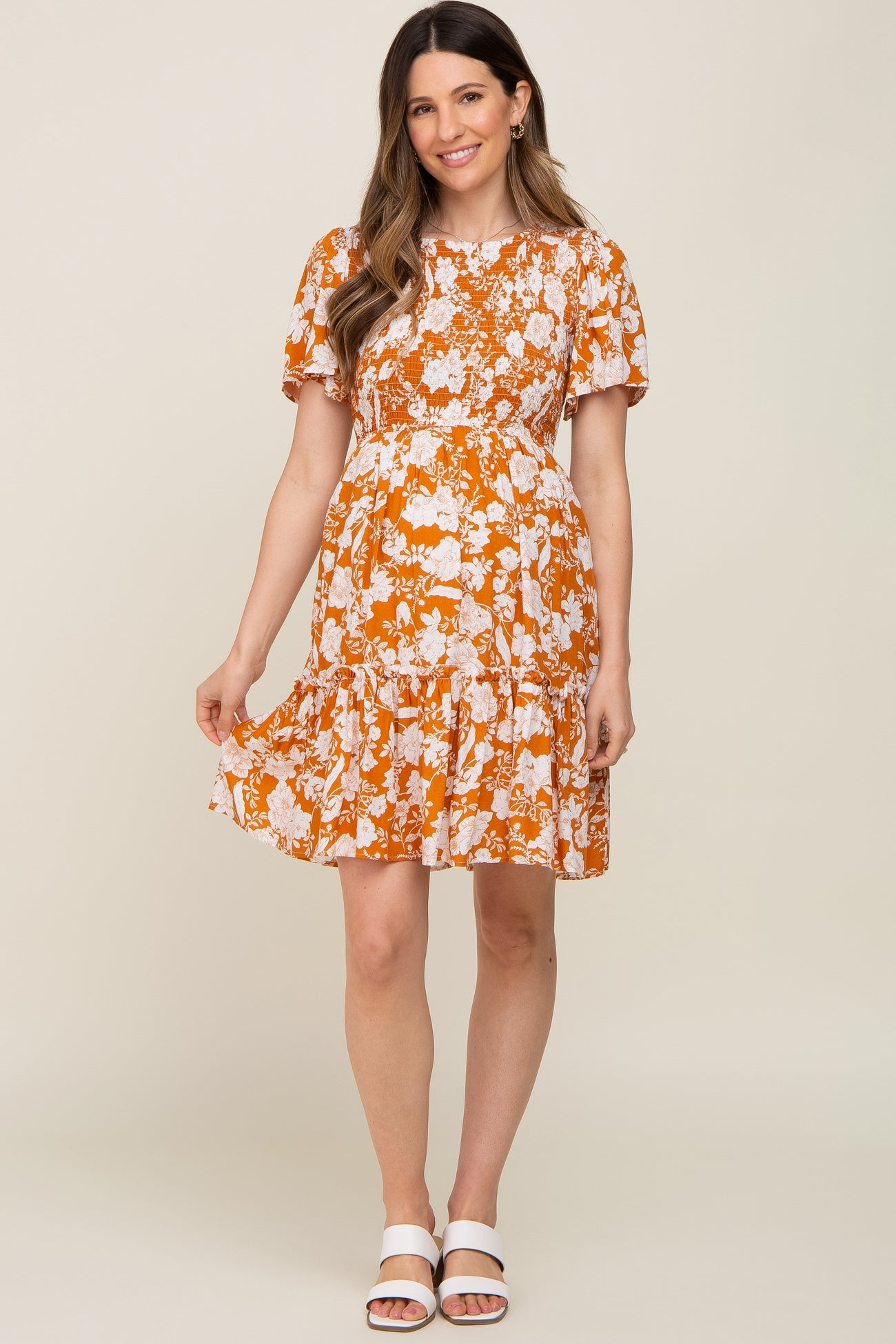 woman wearing an orange floral maternity dress with short puff sleeves and a ruffled hem, showing her baby bump