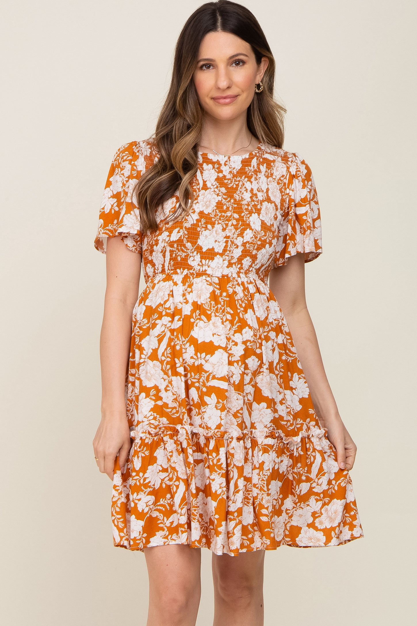 woman wearing an orange floral maternity dress with short sleeves and a tiered skirt, showing her baby bump