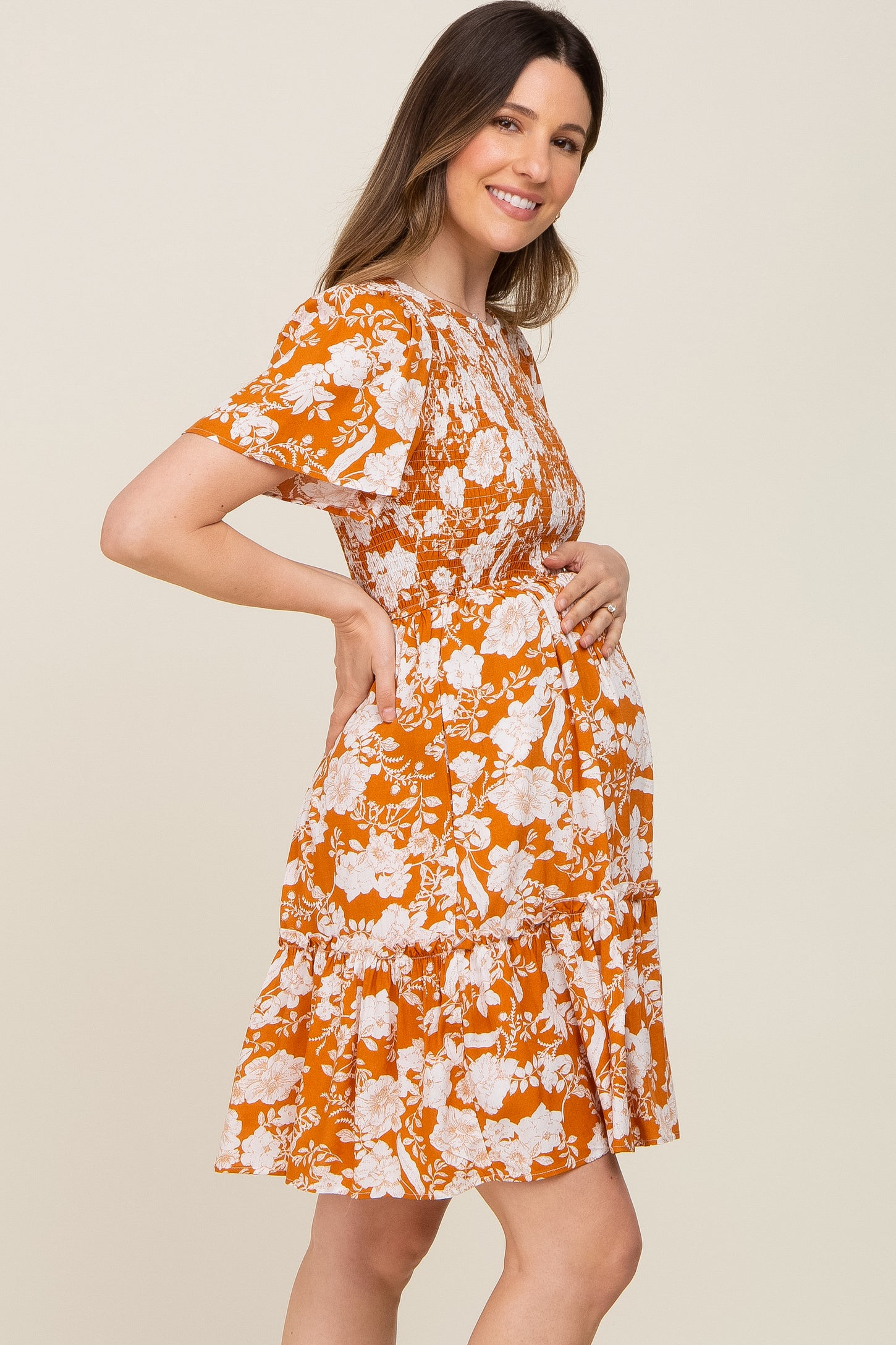 woman wearing an orange floral maternity dress with short sleeves and a tiered skirt, holding her baby bump