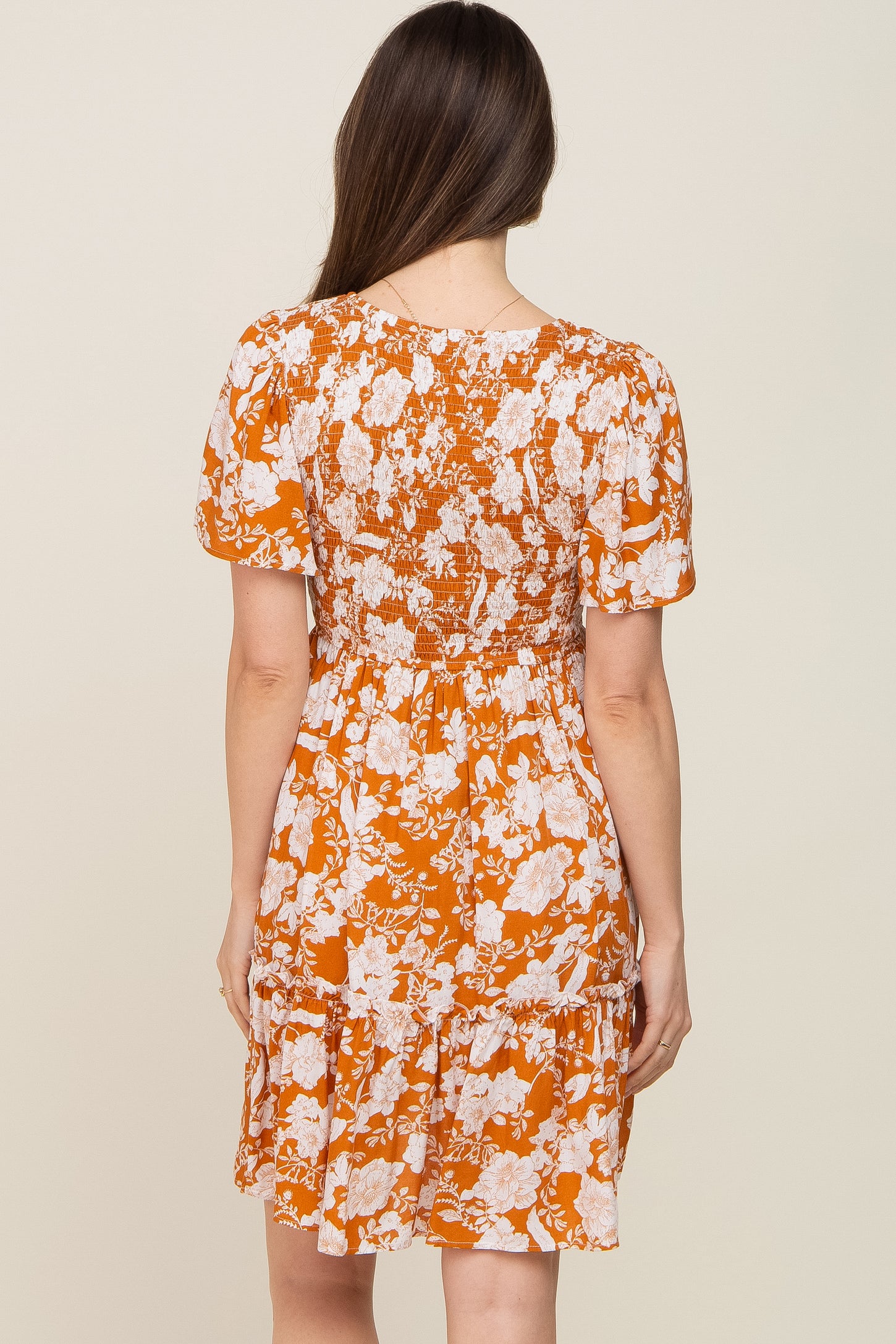 woman wearing an orange floral maternity dress with a smocked back and short sleeves, shown from the back