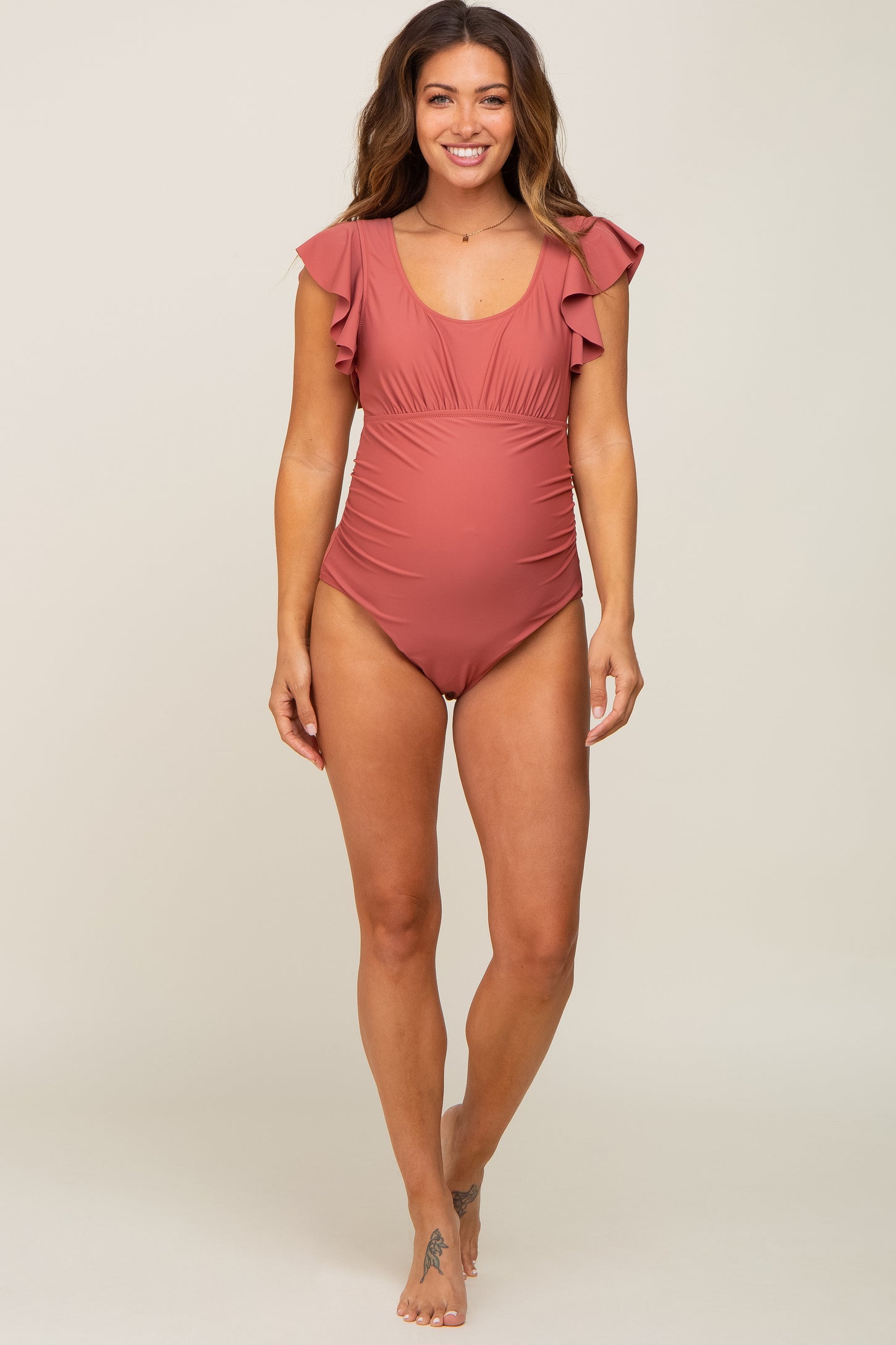 woman wearing a dusty rose maternity swimsuit with ruffle sleeves and a visible baby bump