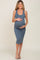 woman wearing a slate blue fitted maternity dress, showing off her baby bump and smiling