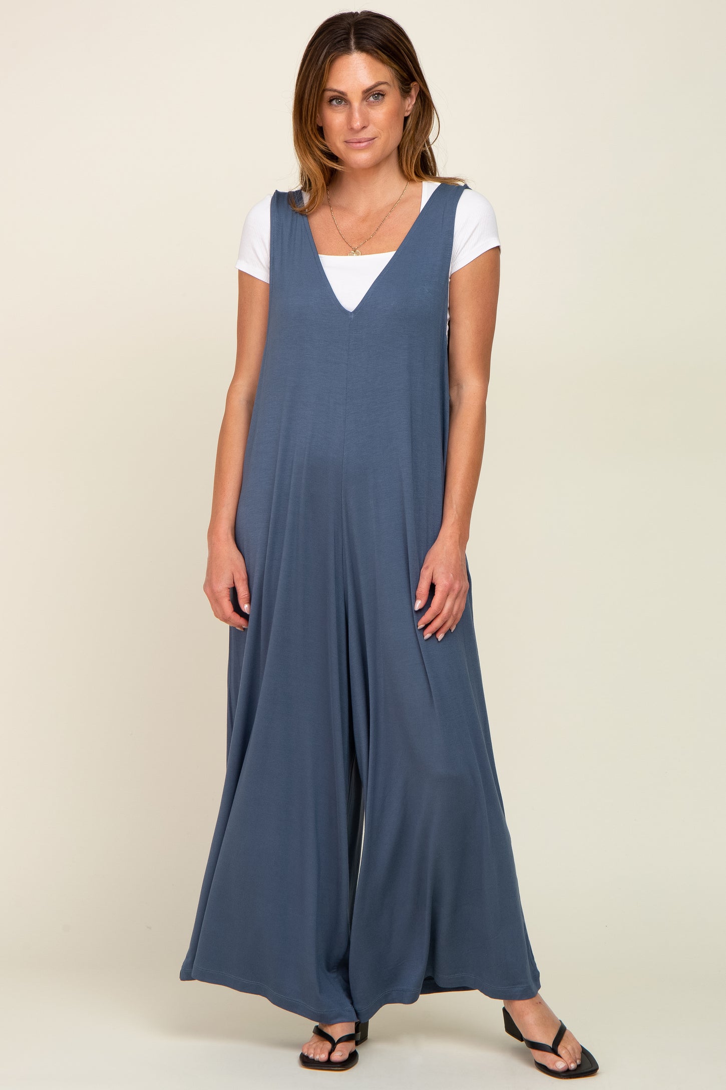 woman wearing a blue sleeveless jumpsuit over a white t-shirt, standing with hands by her sides