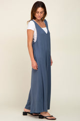 woman wearing a blue sleeveless jumpsuit over a white t-shirt, standing sideways