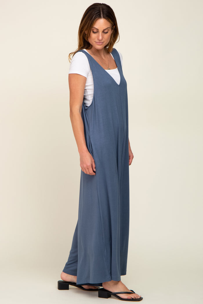 woman wearing a blue sleeveless jumpsuit over a white t-shirt, standing sideways