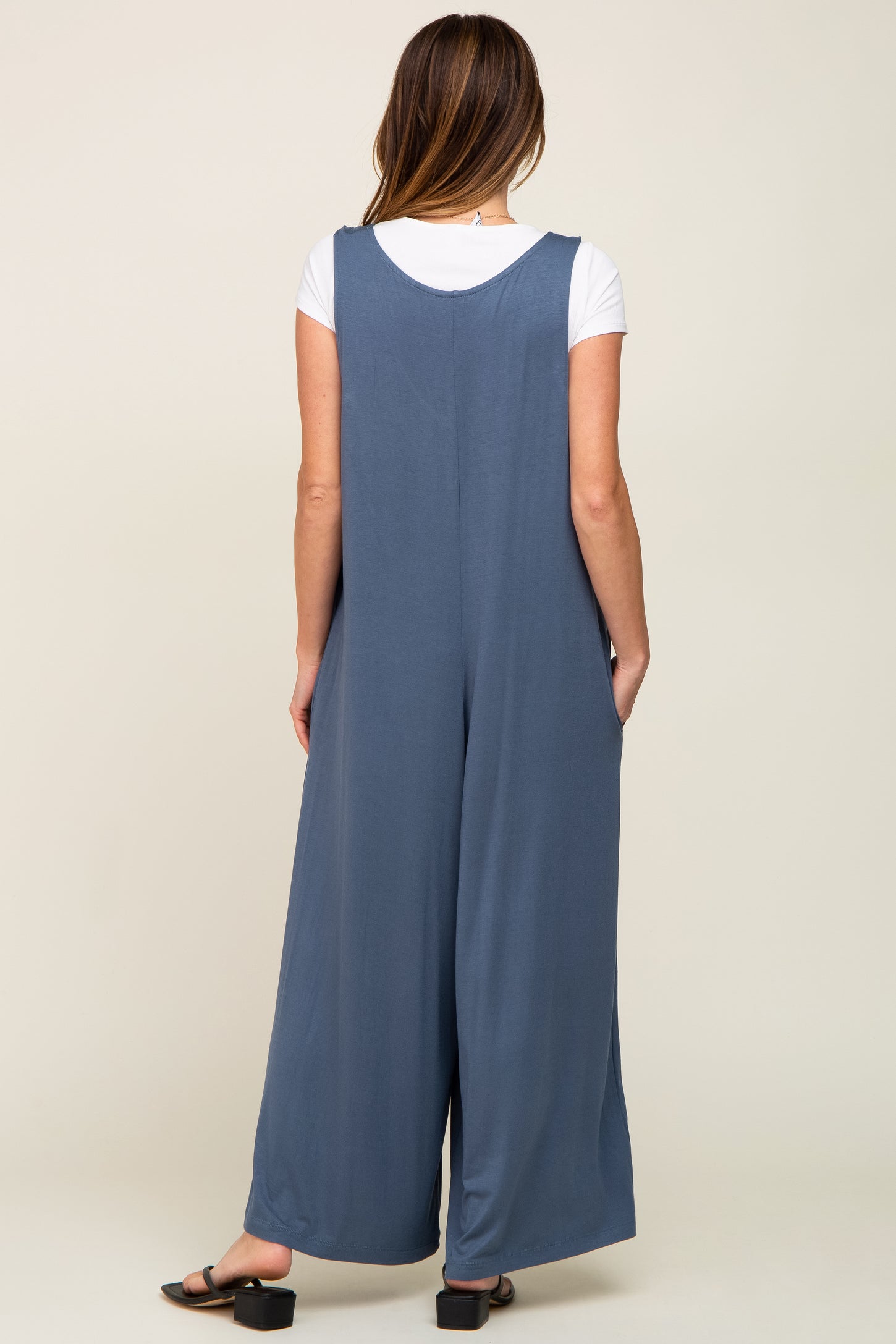 woman wearing a blue sleeveless jumpsuit with wide legs, viewed from the back