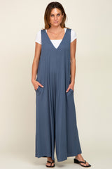 woman wearing a slate blue sleeveless jumpsuit with a deep v-neck and pockets, styled with a white t-shirt underneath